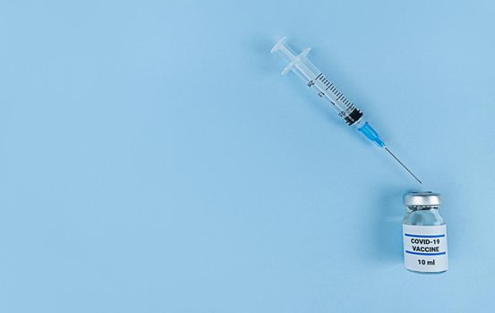 Single use syringe and medical bottle with coronavirus vaccine on a blue background with copy space.