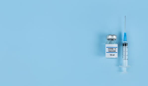 Single use syringe and medical bottle with coronavirus vaccine on a blue background with copy space.