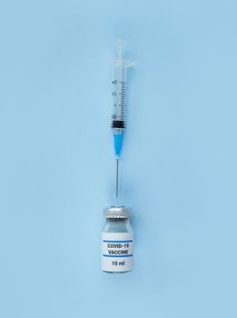 Single use syringe and medical bottle with coronavirus vaccine on a blue background.