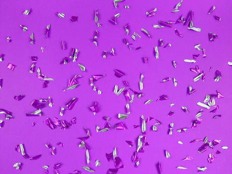 Confetti foil pieces on a purple background. Abstract festive backdrop.