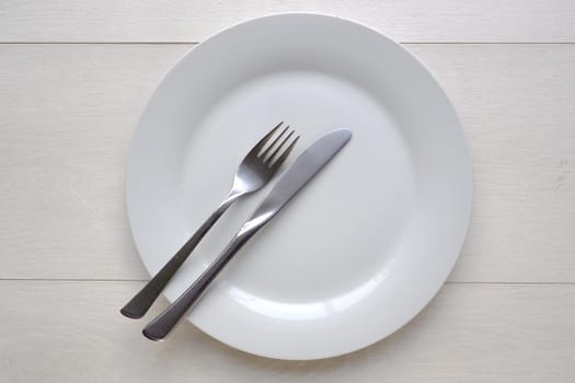 White plate and knife and fork on white wooden background