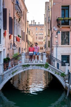 Canals of Venice Italy during summer in Europe,Architecture and landmarks of Venice. Italy Europe, couple mid age men and woman on vacation in Venice relaxing sitting on bridge over canal