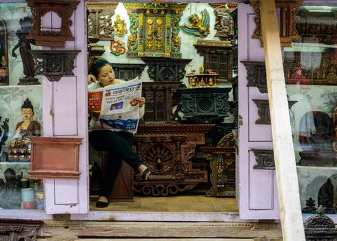 PATAN, NEPAL - CIRCA NOVEMBER 2015: Shopkeeper reading the Kantipur newspaper in her handicraft shop.