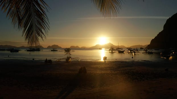 sunset over the beach view through palm tree leaves. Sunset over the sea with islands and boats, Corong corong beach, Palawan, Philippines