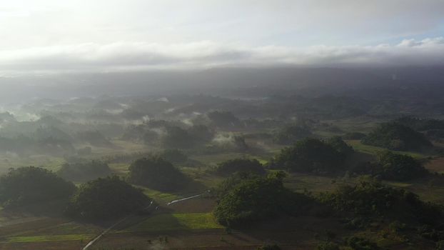 Tropical landscape with farmland and green hills, aerial view. The nature of Luzon Island, Philippines. Fog in the early morning.