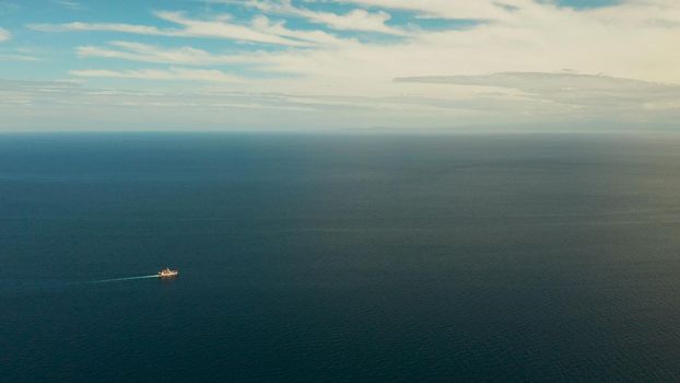 Small passenger ferry cruising in the open blue sea against blue sky with clouds, aerial view. Seascape: assenger ferry boat in open waters Philippines, Mindanao