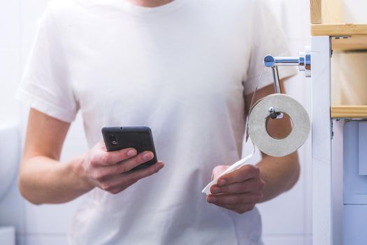 Close up of young man using his smartphone while sitting on the toilet