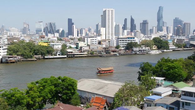 Financial district near calm river. View of skyscrapers located on shore of tranquil Chao Praya river in downtown district of Bangkok. Big city life panorama. Boats on the water in Krungthep