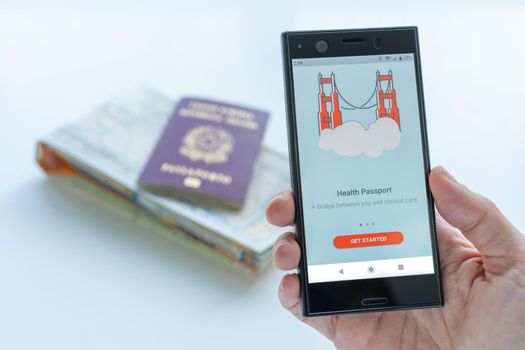 Milan, Italy - 01 26 2020: Digital Health Passport app for smartphone. background with a map and a passport. Coronavirus and traveling concept.