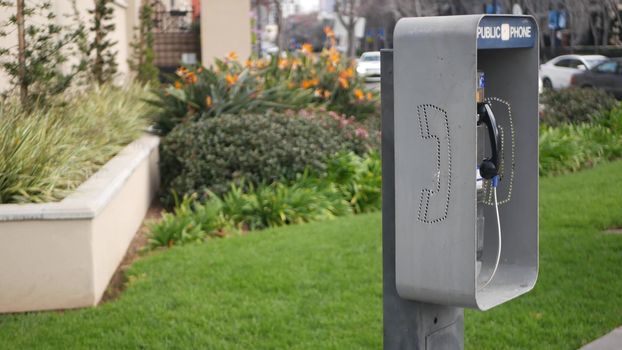 Retro coin-operated payphone station for emergency call on street, California USA. Public analog pay phone booth. Outdated technology for connection and telecommunication service. Cell handset on box.