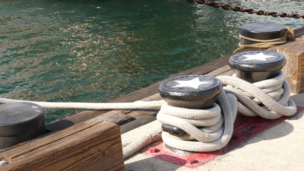 Tied rope knot on metallic bollard with stars, seafaring port of San Diego, California. Nautical ship moored in dock. Cable tie fixed on wharf. Symbol of navy marine sailing and naval fleet, USA flag.