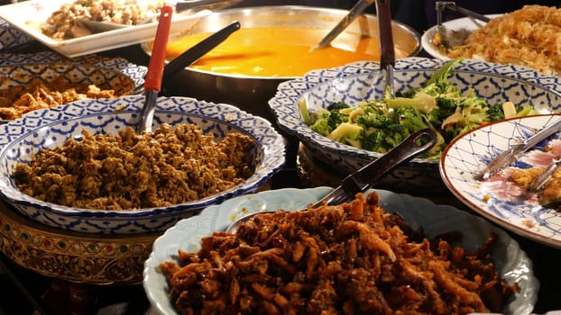 Bowls with various Asian dishes on stall. Bowls of assorted traditional Thai dishes placed on stall of street diner in evening. Oriental night market food court