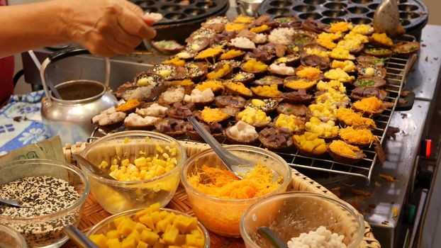 Exotic Oriental Asian sweet delicious desserts, unusual colorful traditional dishes on the counters of a bazar with street food. Evening food court in bangkok, the capital of cooking. Night market