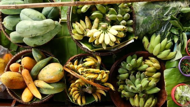 Iconic asian Lat Mayom floating market. Khlong river canal, long-tail boat with tropical exotic colorful fruits, organic locally grown vegetables. Top view of harvest and street food in wooden canoe.