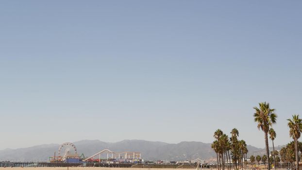 California beach aesthetic, classic ferris wheel, amusement park on pier, Santa Monica pacific ocean resort. Summertime iconic view, palm trees and sky, symbol of Los Angeles with copy space, CA USA.