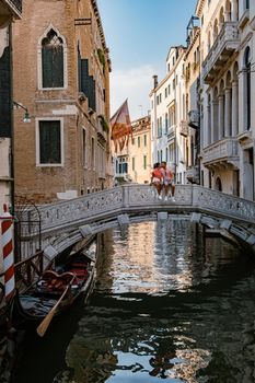 Canals of Venice Italy during summer in Europe,Architecture and landmarks of Venice. Italy Europe, couple mid age men and woman on vacation in Venice relaxing sitting on bridge over canal