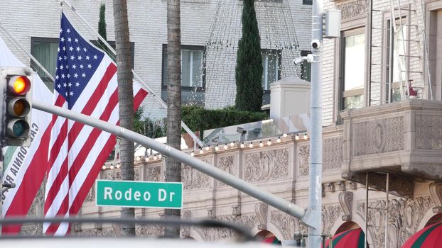 World famous Rodeo Drive Street Road Sign in Beverly Hills against American Unated States flag. Los Angeles, California, USA. Rich wealthy life consumerism, Luxury brands, high-class stores concept