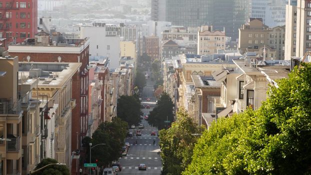 Iconic hilly street and crossroads in San Francisco, Northern California, USA. Steep downhill road and pedestrian walkway. Downtown real estate, victorian townhouses abd other residential buildings.