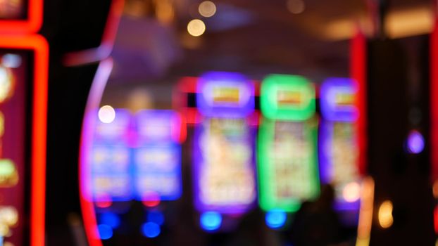 Defocused slot machines glow in casino on fabulous Las Vegas Strip, USA. Blurred gambling jackpot slots in hotel near Fremont street. Illuminated neon fruit machine for risk money playing and betting.