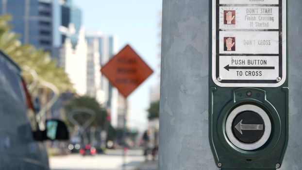 Traffic light button on pedestrian crosswalk, people have to push and wait. Traffic rules and regulations for public safety in USA. Zebra street crossing on road intesection in San Diego, California.