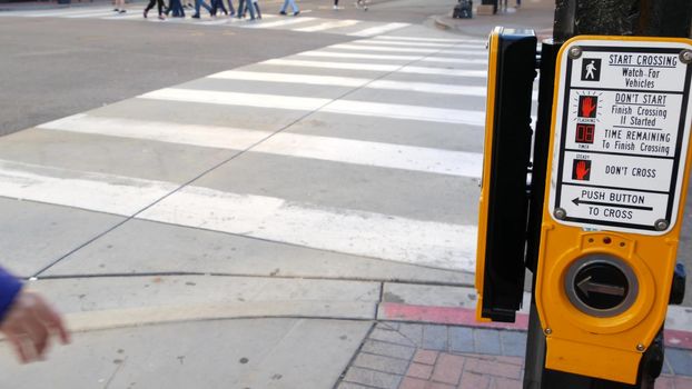 Traffic light button on pedestrian crosswalk, people have to push and wait. Traffic rules and regulations for public safety in USA. Zebra street crossing on road intesection in San Diego, California.