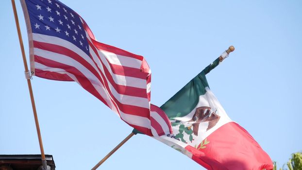 Mexican tricolor and American flag waving on wind. Two national icons of Mexico and United States against sky, San Diego, California, USA. Political symbol of border, relationship and togetherness.