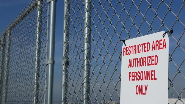 Restricted area, authorized personnel only sign in USA. Red letters, keep off warning on metal fence, United States border symbol. No trespassing notice means violators will be prosecuted by US law.