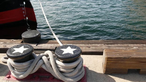 Tied rope knot on metallic bollard with stars, seafaring port of San Diego, California. Nautical ship moored in dock. Cable tie fixed on wharf. Symbol of navy marine sailing and naval fleet, USA flag.
