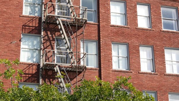 Fire escape ladder outside residential brick building in San Diego city, USA. Typical New York style emergency exit for safe evacuation. Classic retro house exterior as symbol of real estate property.