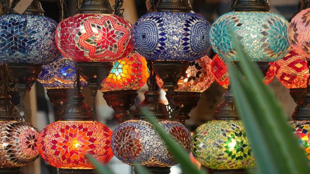 Colourful turkish lamps from glass mosaic glowing. Arabic multi colored authentic retro style lights. Many illuminated moroccan craft lanterns. Oriental islamic middle eastern decor. Shiny folk shop.