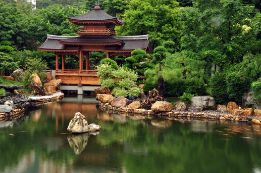 Tranquil oriental garden with pond, Zen view of calm green pond water with oriental house and rocks on shore, Hong Kong, Nan Lian