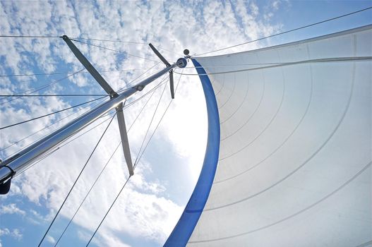 From below shot of white waving sail on tall mast under blue sky in clouds . White sail on mast under blue sky