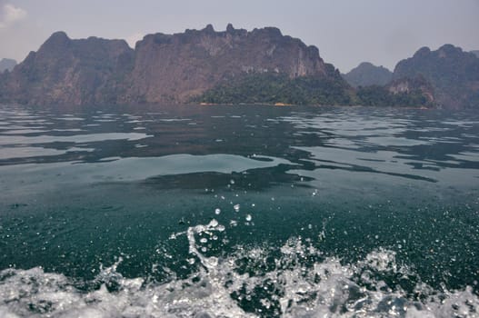 Splashing waves of tropical bay with karst cliffs, Clear fresh splashes of waves of blue clear water with rocky cliffs on background, Thailand, Khao Sok National park.