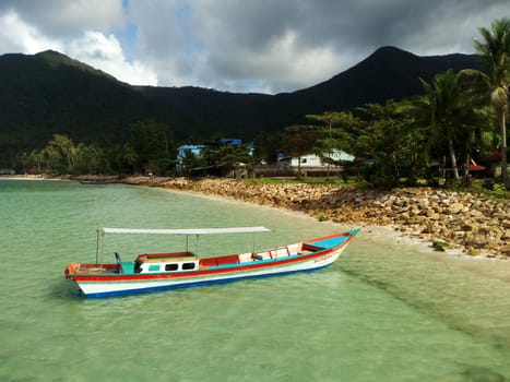 View of single floating fisherman boat in crystal water of tropical coastline with mountains and palms. Sailing boat in clear water of ocean. Koh Phangan exotic paradise island