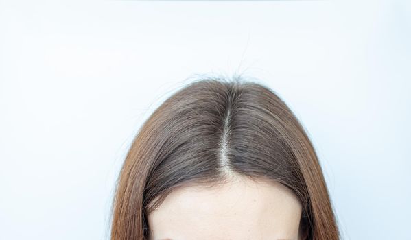 A woman's head with a parting of gray hair that has grown roots due to quarantine. Brown hair on a woman's head close-up.