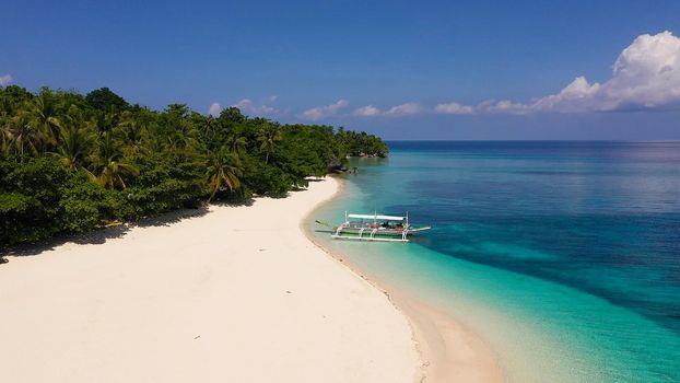 Tropical beach of white sand, top view. Tranquil beach scene. Tourist boat off the coast. Blue sea with turquoise lagoons. Coral reef near the beach. Summer and travel vacation concept.