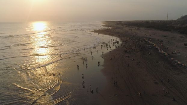 sandy beach parangtritis near ocean with big waves, people in tropical resort at sunset. Yogyakarta, Indonesia. aerial view seascape, ocean and beautiful beach. Travel concept. Indonesia, jawa