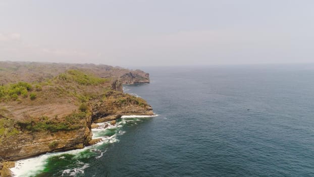 aerial view rocky coastline with cliffs, ocean surf with breaking waves in coast. seascape waves break on rocky shore java, indonesia