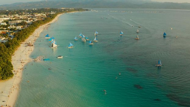 Topical white beach from above at sunset with tourists and sailing yachts on Boracay Island. Tropical white beach with sailing boat. Summer and travel vacation concept.