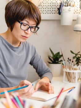 Woman with short hair cut is drawing in notebook. Calming hobby, anti stress leisure. Artist at work. Cozy workplace.