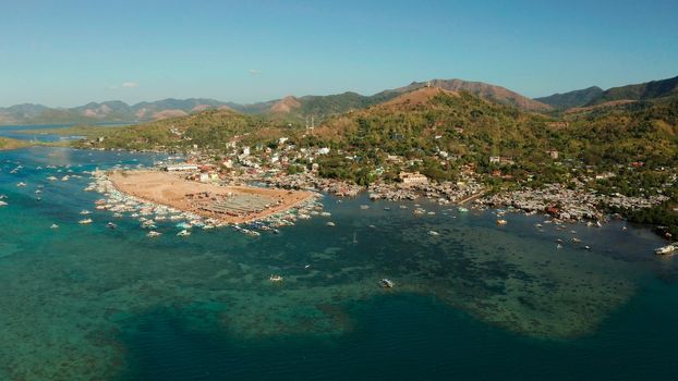 aerial view City Quay with boat dock and public market Coron town, tourist destination in the Philippines. Pier and promenade with boats on Busuanga island. Wooden boats waiting at pier. Seascape with mountains.