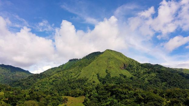 Hills with green grass and blue sky with white puffy clouds. Beautiful landscape on the island of Luzon, aerial view.