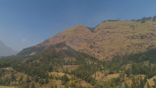 mountains with farmlands, village, fields with crops, trees. Aerial view mountain landscape slopes mountains covered with green forest. Java, Indonesia.