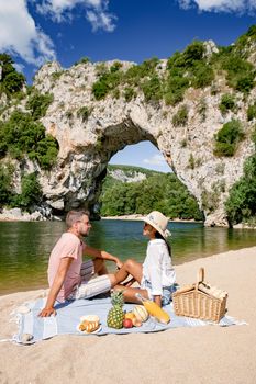 couple men and woman picnic on the beach of the The famous natural bridge of Pont d'Arc in Ardeche department in France Ardeche. Europe Rhone Alpes