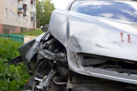 close-up view on front right side of silver car physically damaged in road accident, close-up with blurry background.