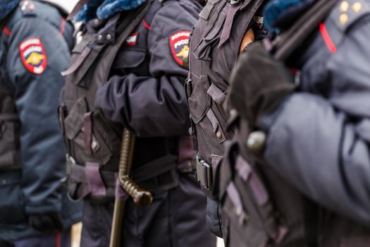 Tula, Russia - January 23, 2021: Police officers in black uniform with bulletproof vests - close-up view on black gloves with background blur.