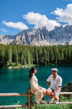 The majestic Lake of Lago di Carezza, beautiful green and turquoise colors in Dolomites mountains Italy,South tyrol, Italy. Landscape of Lake Carezza or Karersee couple men woman hiking