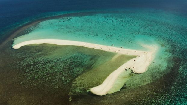 Tropical white island and sandy beach with tourists surrounded by coral reef and blue sea, aerial view. Sandbar Atoll. Island with sand bar and coral reef. Summer and travel vacation concept, Camiguin, Philippines.