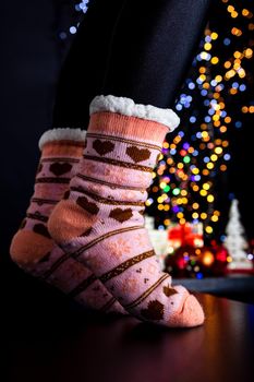 Female legs in Christmas colorful socks near Christmas tree.