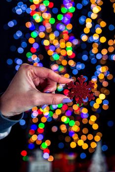 Holding Christmas snowflake decoration isolated on background with blurred lights. December season, Christmas composition.